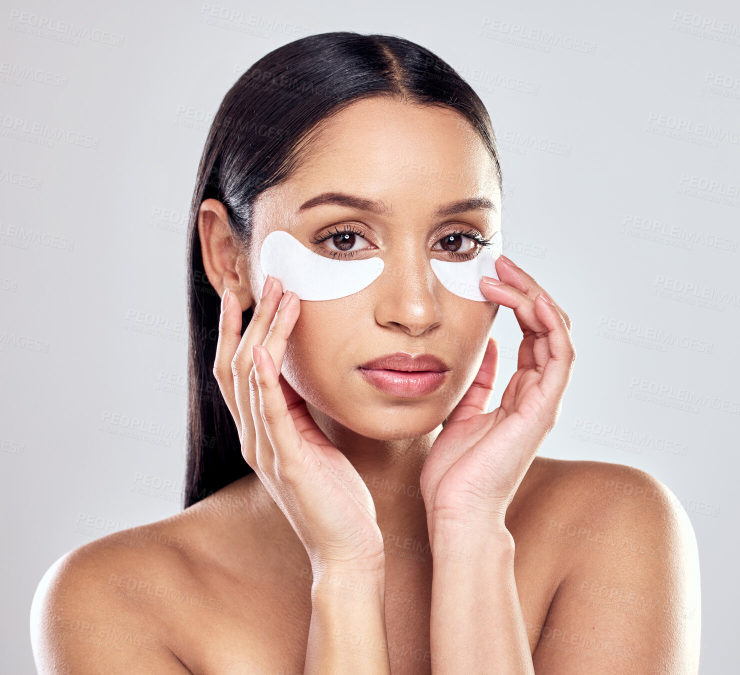 Buy stock photo Shot of a young woman using eye masks against a studio background