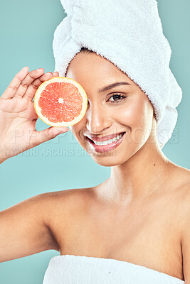 Buy stock photo Shot of a young woman covering her eye with a slice of grapefruit against a studio background