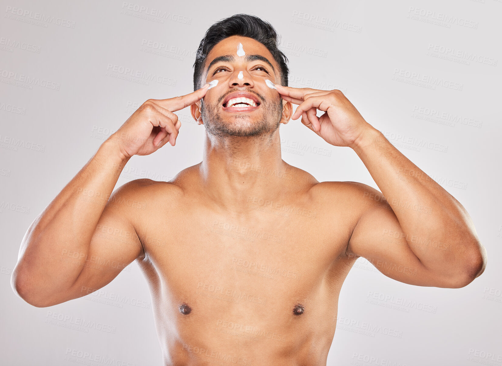 Buy stock photo Shot of a young man applying lotion to his face against a grey background