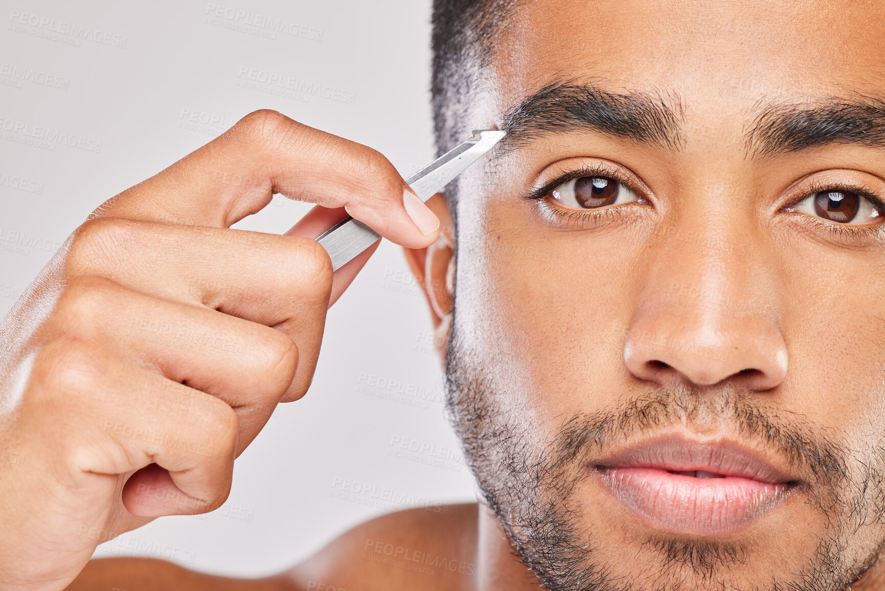 Buy stock photo Shot of a young man plucking his eyebrows against a grey background