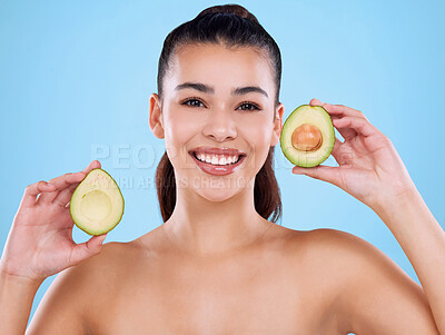 Buy stock photo Studio portrait of an attractive young woman posing with two halves of an avo against a blue background