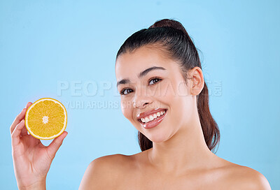 Buy stock photo Studio portrait of an attractive young woman posing with half an orange against a blue background