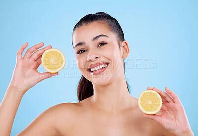 Buy stock photo Studio portrait of an attractive young woman posing with two halves of a lemon against a blue background