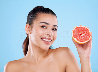 Buy stock photo Studio portrait of an attractive young woman posing with half a grapefruit against a blue background