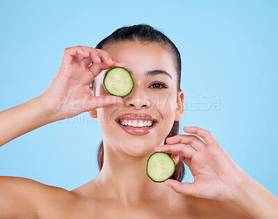 Buy stock photo Studio portrait of an attractive young woman posing with two slices of cucumber against a blue background