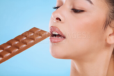 Buy stock photo Studio shot of an attractive young woman biting into slab of chocolate against a blue background