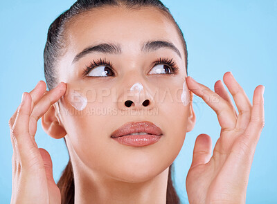 Buy stock photo Studio shot of an attractive young woman applying moisturizer against a blue background