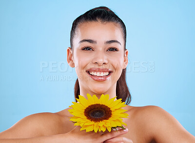 Buy stock photo Studio portrait of an attractive young woman posing with a sunflower against a blue background