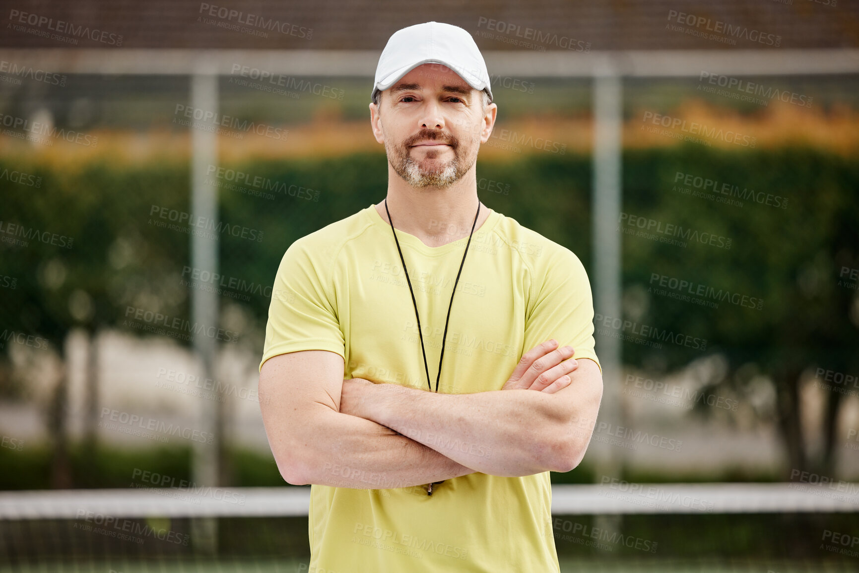 Buy stock photo Cropped portrait of a handsome mature male tennis coach standing with his arms folded on the court