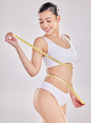 Buy stock photo Studio shot of a fit young woman holding a measuring tape around her waist