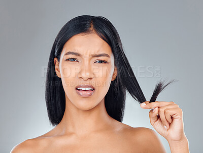 Buy stock photo Studio portrait of an attractive young woman looking upset while holding the ends of her hair against a grey background