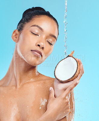 Buy stock photo Shot of a young female holding a coconut while taking a shower against a blue background