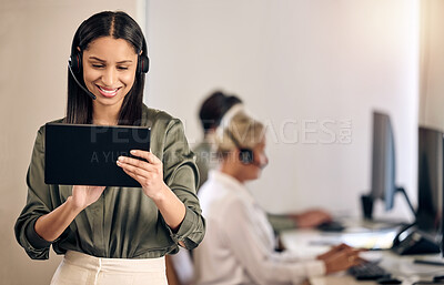 Buy stock photo Shot of a young call centre agent using a digital tablet while working in an office with her colleagues in the background