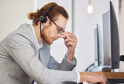 Buy stock photo Shot of a handsome customer service agent sitting alone in his office and feeling stressed while using his computer