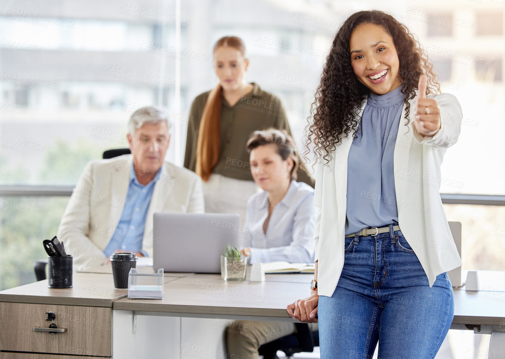 Buy stock photo Shot of an attractive young businesswoman standing and showing a thumbs up while her colleagues work behind her