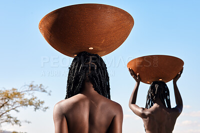 Buy stock photo Rearview shot of two unrecognizable young women carrying pots on their heads outside