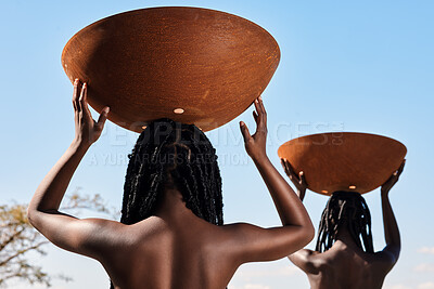 Buy stock photo Rearview shot of two unrecognizable young women carrying pots on their heads outside