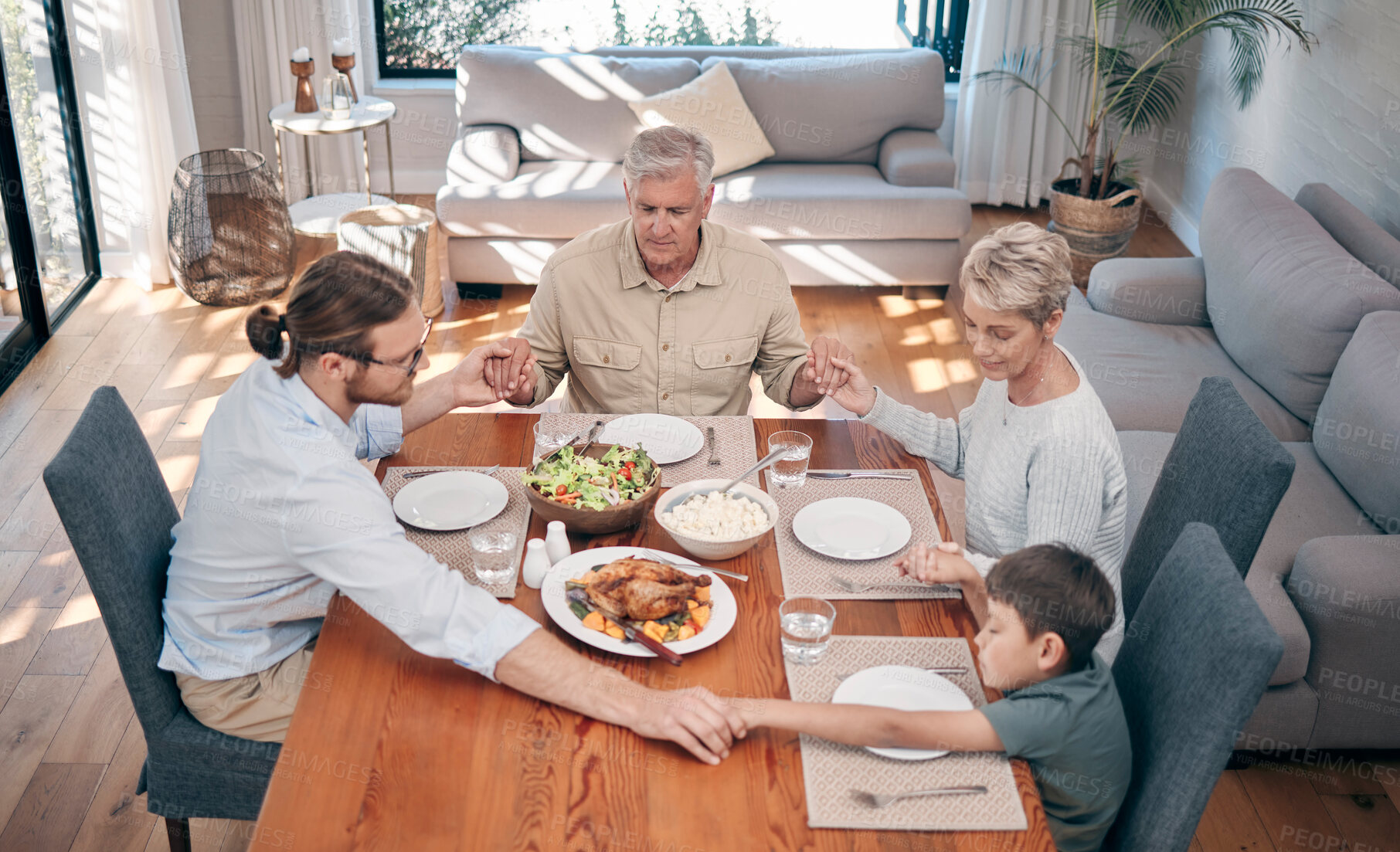 Buy stock photo Shot of a family holding hands in prayer before having a meal together at home