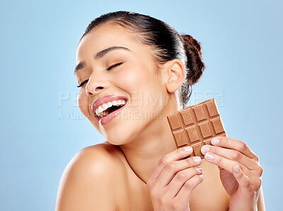 Buy stock photo Studio shot of an attractive young woman eating a slab of chocolate against a blue background