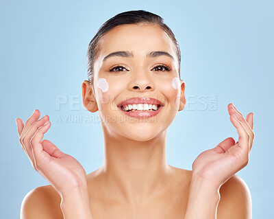 Buy stock photo Studio portrait of an attractive young woman applying moisturiser on her face against a blue background