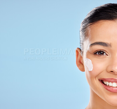 Buy stock photo Studio portrait of an attractive young woman posing with moisturiser on her face against a blue background