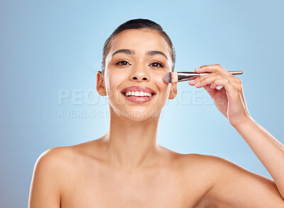 Buy stock photo Studio portrait of an attractive young woman applying makeup to her face with a brush against a blue background