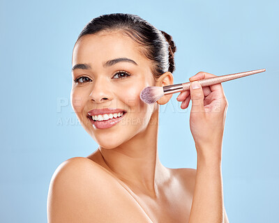 Buy stock photo Studio portrait of an attractive young woman applying makeup to her face with a brush against a blue background