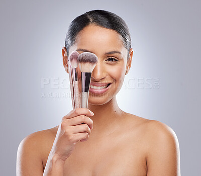 Buy stock photo Shot of an attractive young woman standing alone in the studio and feeling playful while holding makeup brushes
