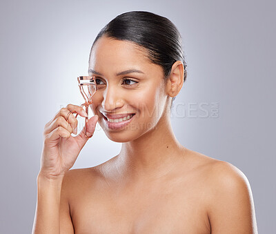 Buy stock photo Shot of an attractive young woman standing alone in the studio and using an eyelash curler