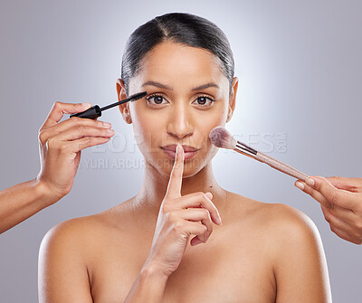 Buy stock photo Shot of an attractive young woman posing with her finger over her lips while she gets her makeup done