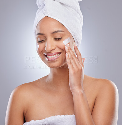 Buy stock photo Shot of an attractive young woman applying moisturiser to her skin in the studio
