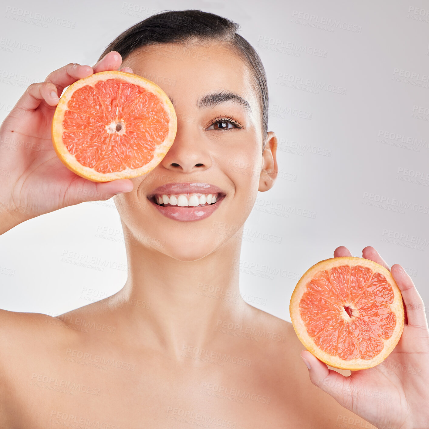 Buy stock photo Studio portrait of a young woman posing with half a grapefruit against a grey background