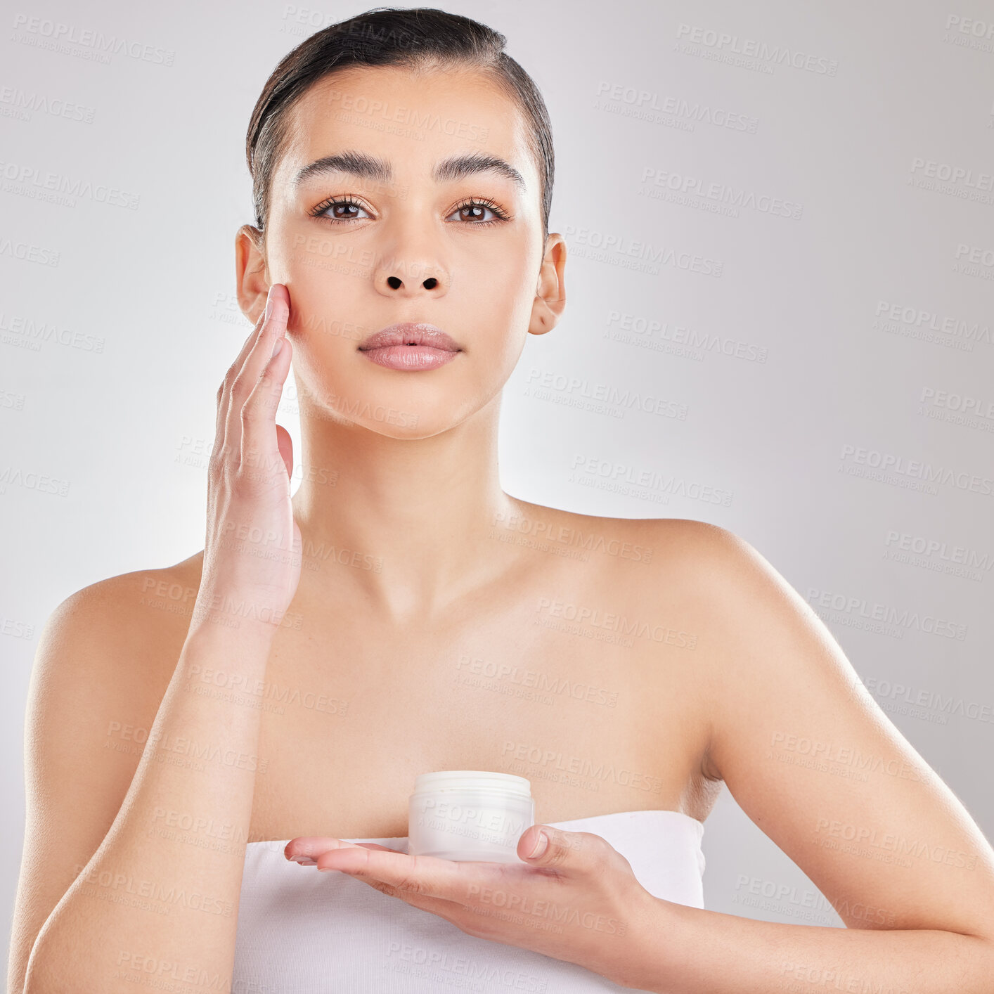 Buy stock photo Shot of a young woman applying a cream to her face against a grey background