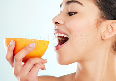Buy stock photo Studio shot of an attractive young woman biting into an orange against a light background