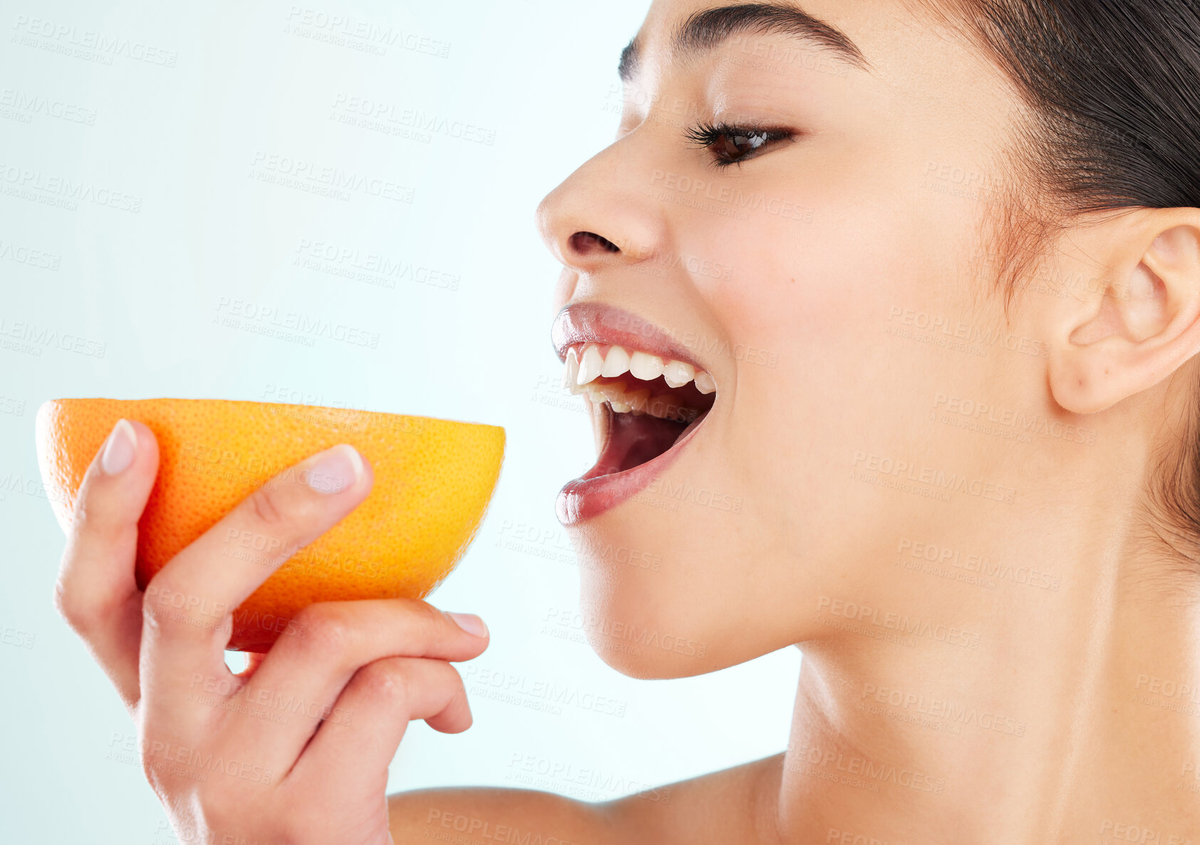 Buy stock photo Studio shot of an attractive young woman biting into an orange against a light background