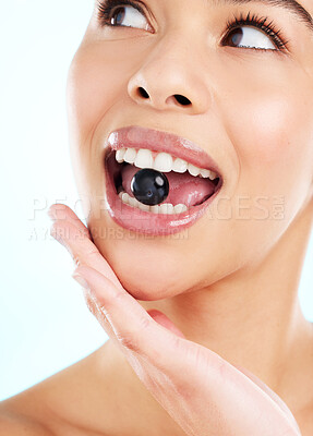 Buy stock photo Studio shot of an attractive young woman biting a black current against a light background