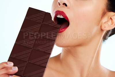 Buy stock photo Studio shot of an unrecognizable young woman biting into a slab of chocolate against a light background