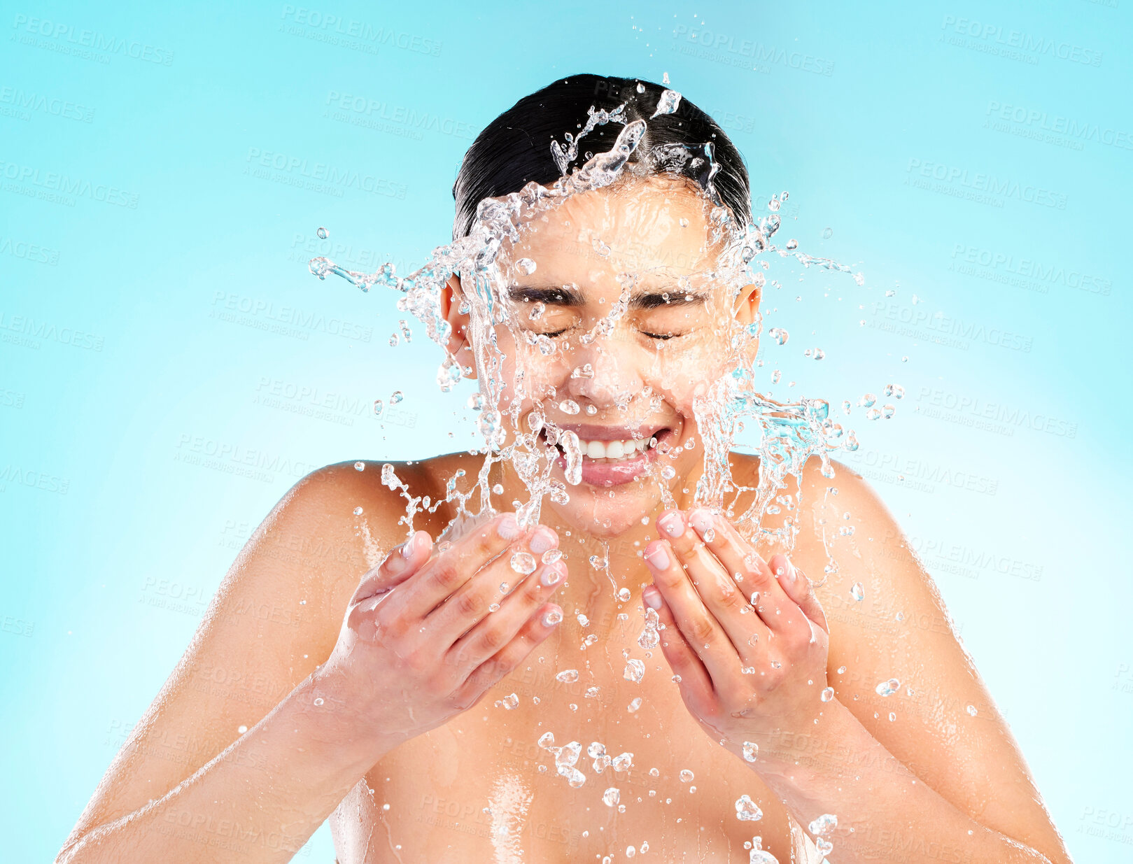 Buy stock photo Happy, woman and water drops or splash in studio for skincare, dermatology and glow or wellness. Hygiene, model girl and smile or hands or liquid for facial and aesthetic or clean by blue background 