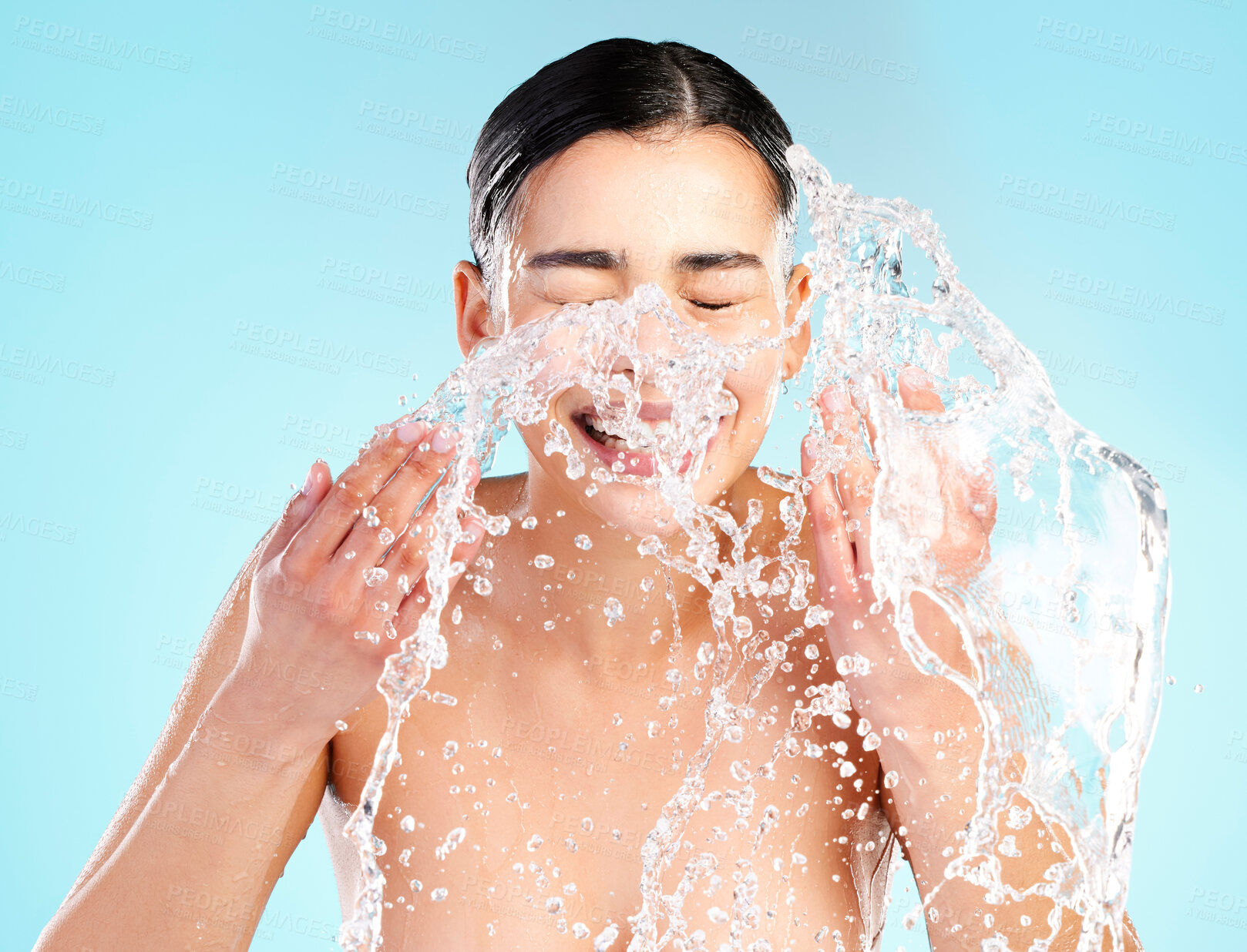 Buy stock photo Happy, woman and splash or skincare in studio with water, dermatology and cleaning or wellness. Hygiene, model girl and smile or hands and liquid for facial, aesthetic and shine by blue background 