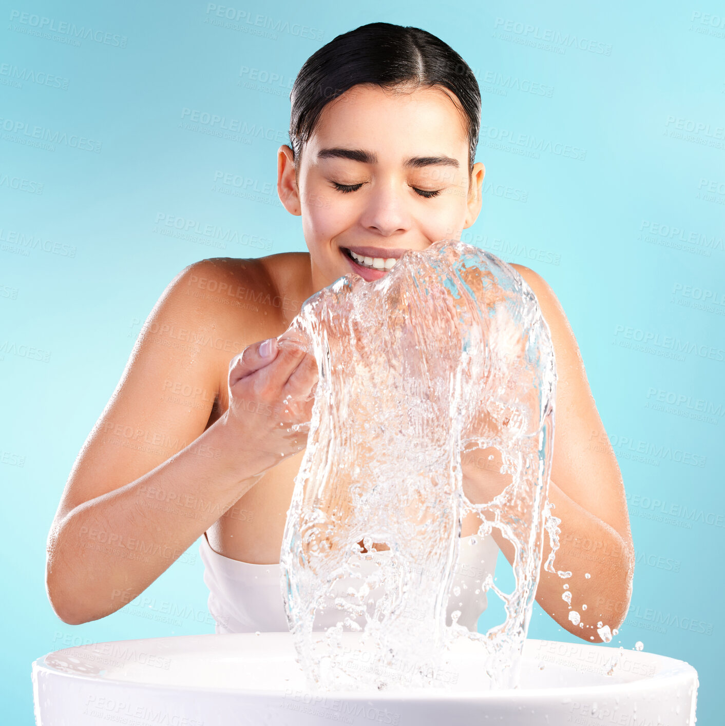 Buy stock photo Happy, woman and dermatology or water in studio for skincare, splash and glow for wellness. Hygiene, model girl and smile of hands with liquid for facial and aesthetic or shine by blue background 