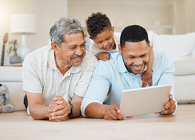 Buy stock photo Shot of a mature man laying with his son and his grandson on the floor while using a tablet at home