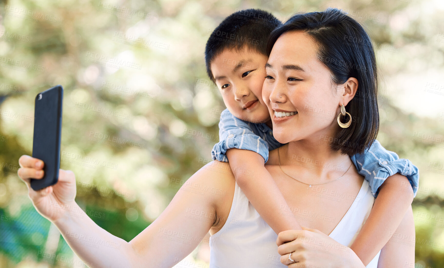 Buy stock photo Shot of a happy young mother and her adorable little boy taking selfies in a garden