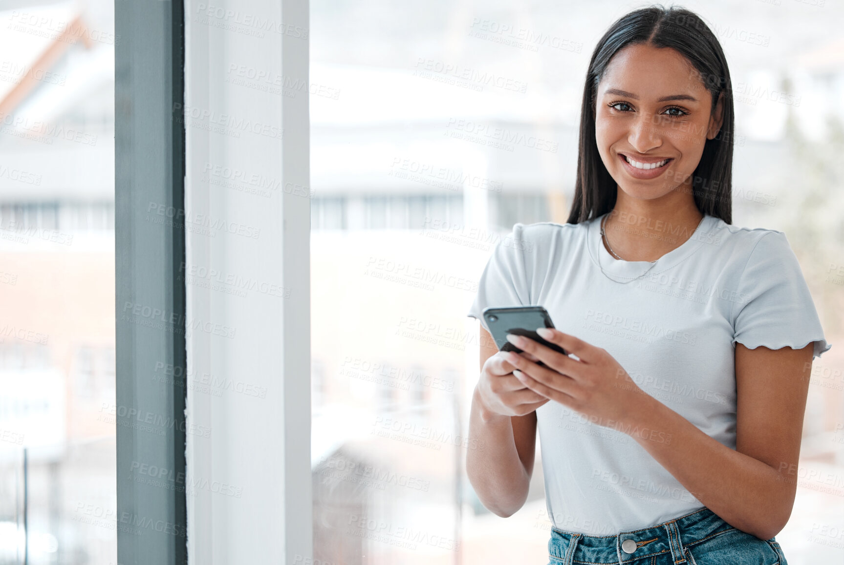 Buy stock photo Shot of an attractive young woman standing alone at home and using her cellphone