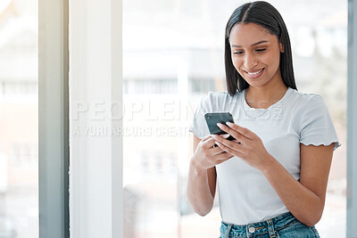 Buy stock photo Shot of an attractive young woman standing alone at home and using her cellphone