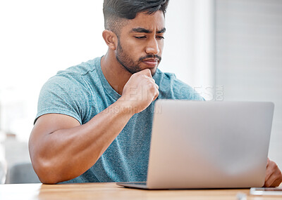 Buy stock photo Shot of a handsome young man sitting alone at home and looking contemplative while using his laptop