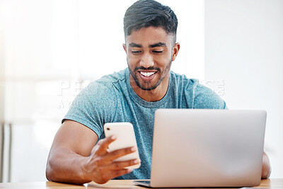 Buy stock photo Shot of a handsome young man sitting alone at home and using technology