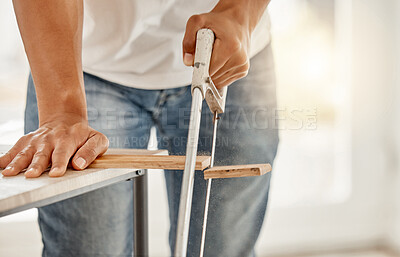 Buy stock photo Cropped shot of an unrecognisable man standing alone and using a saw to cut a beam of wood