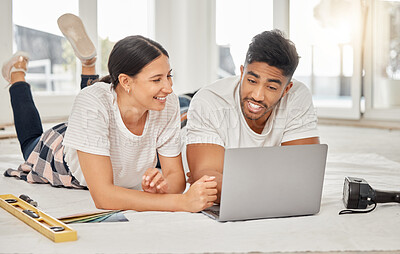 Buy stock photo Shot of a young couple lying on their living room floor and using a laptop