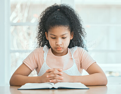 Buy stock photo Shot of a focused little girl praying while reading a bible at the table at home