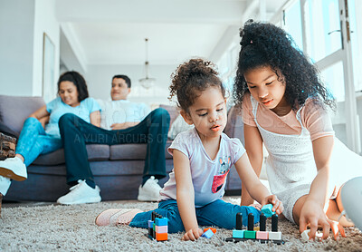 Buy stock photo Shot of two sister playing on the floor while their parents relax in the background